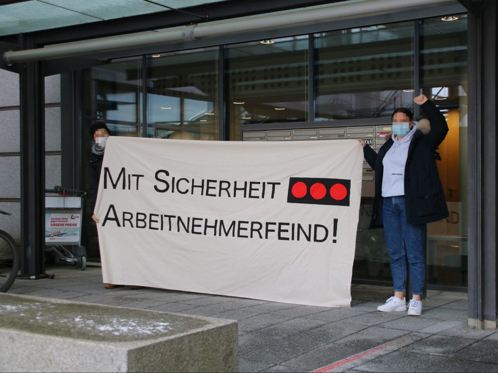 Zwei Aktivistinnen stehen vor der Geschäftsstelle von Securitas in Stuttgart. Sie halten ein Transparent mit der Aufschrift "Mit Sicherheit Arbeitnehmerfeind" und dem Logo von Securitas